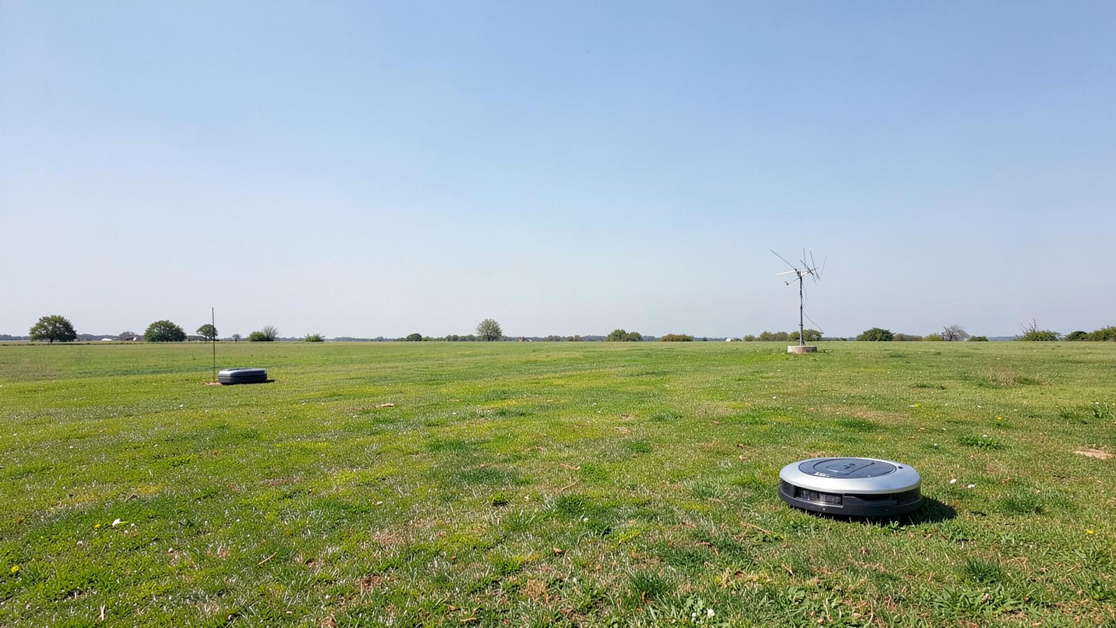 Wire-free robotic mower beside a satellite reference antenna on a lawn