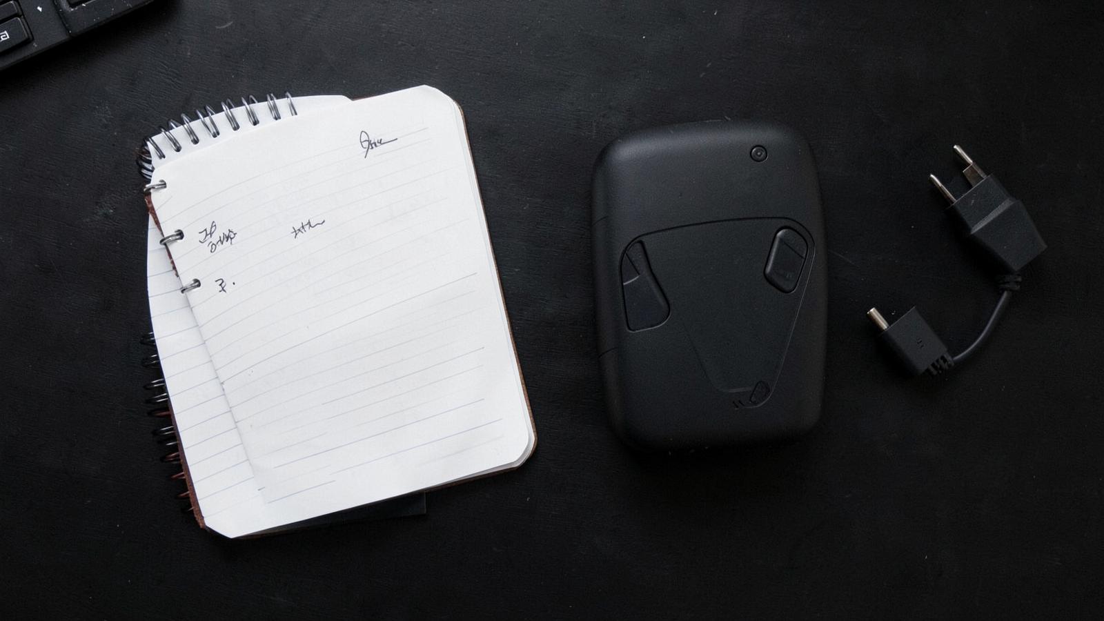Portable power station beside a notebook and plug adapter on a dark desk