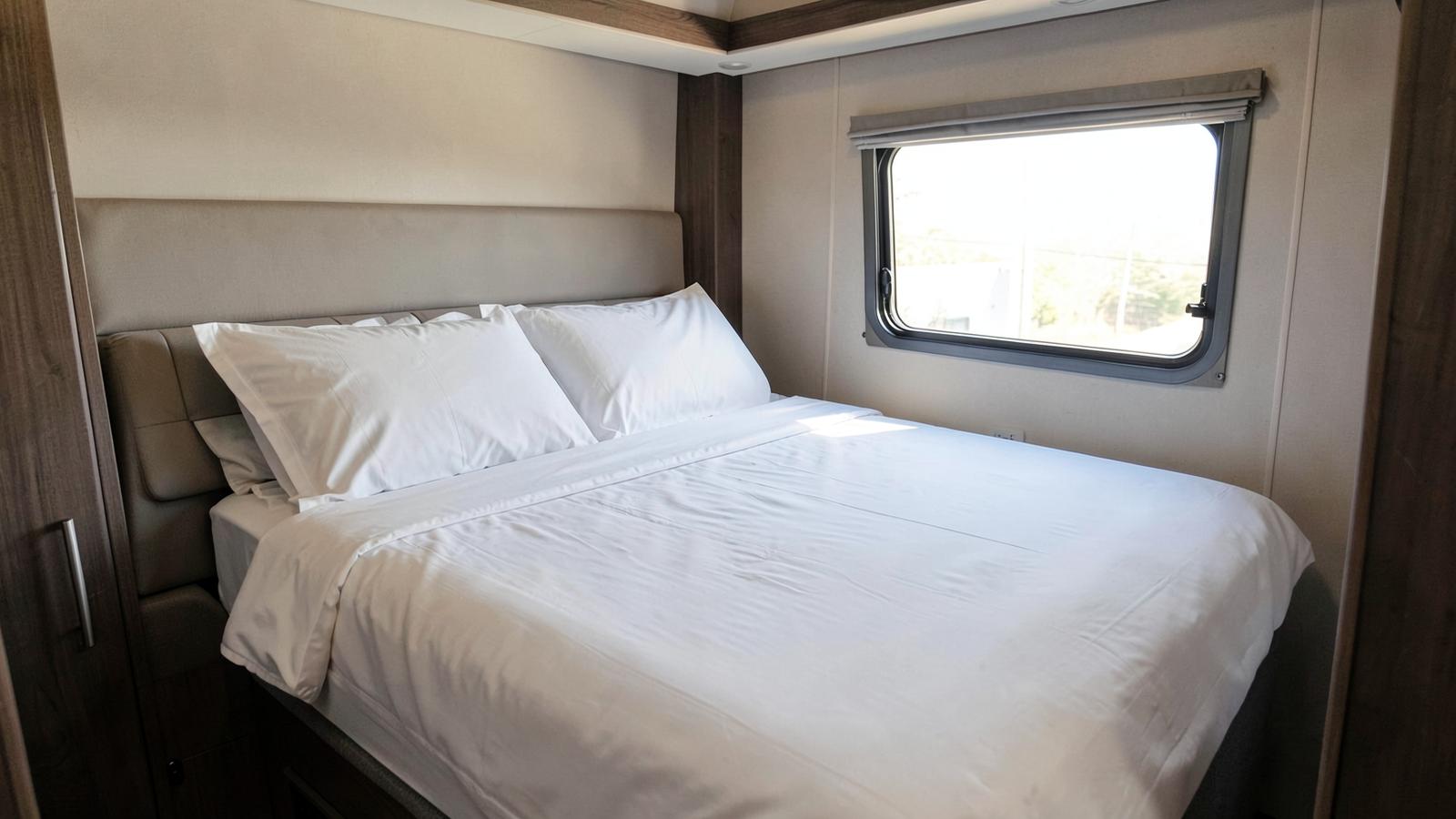 Neatly made bed with white linens in a compact RV bedroom