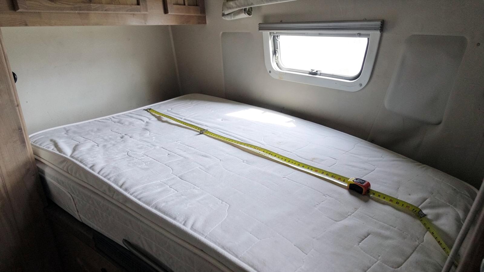 Tape measure stretched across a bare mattress in a compact RV bedroom