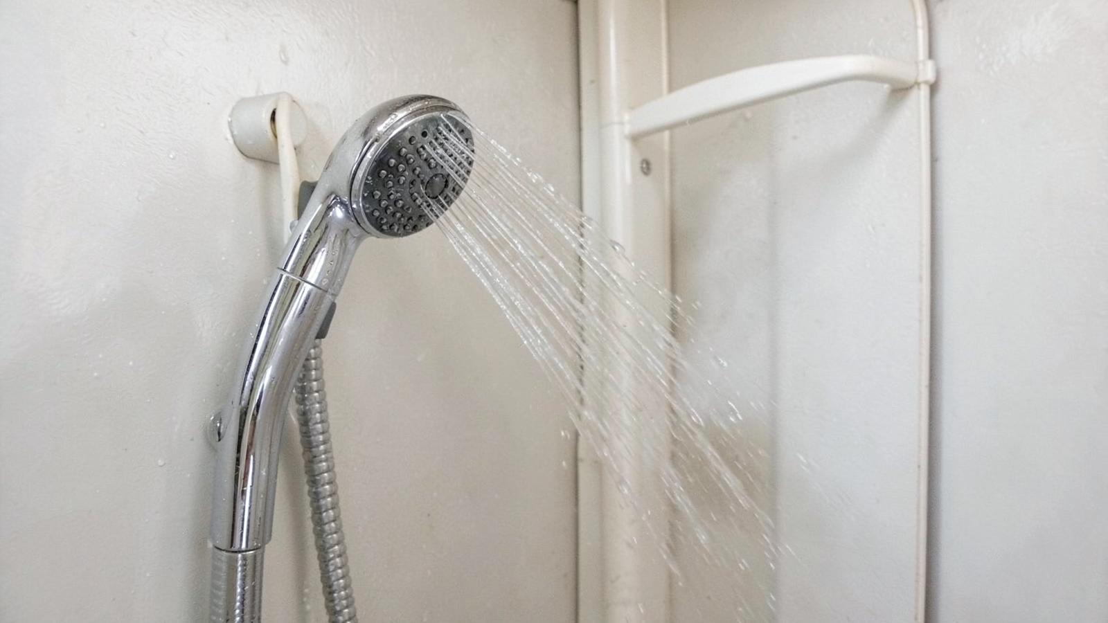 Handheld shower head spraying water in a compact RV shower stall